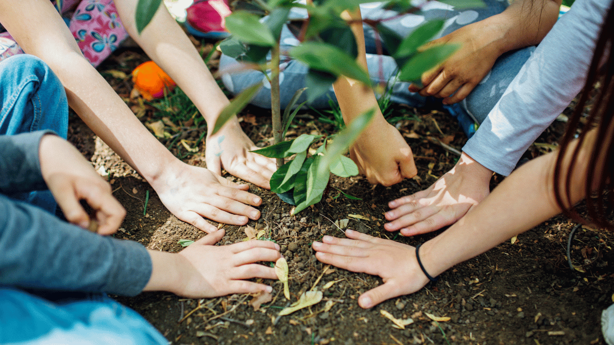 Giving USA 2025 Blog Header. Description: group of children working collaboratively to plant a tree in rich, earthy soil