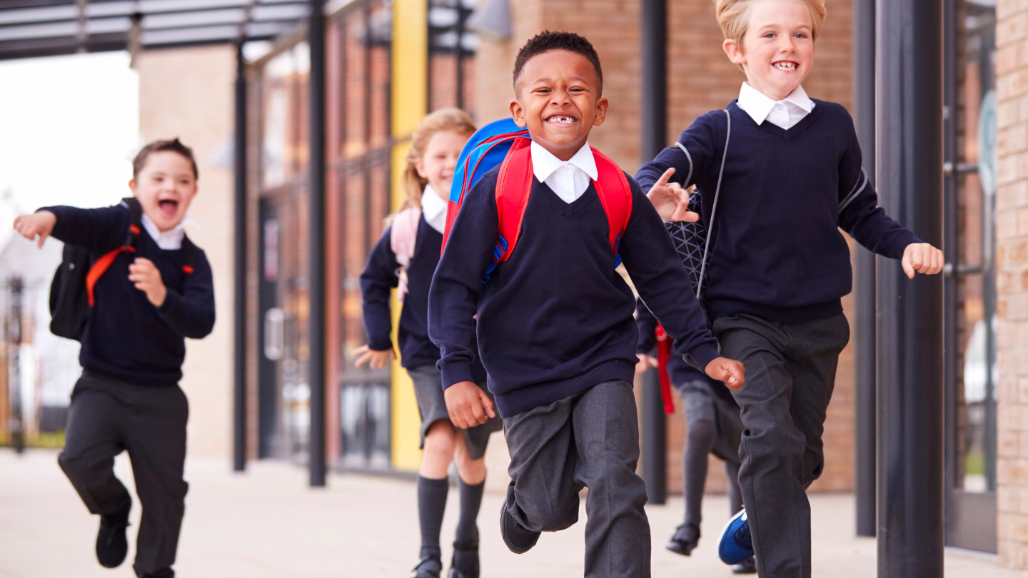 Header image for blog, "How Independent Schools Can Make Strategic Plans that Deliver." The image features elementary schoolchildren running in a corridor. They have on school uniforms and backpacks.